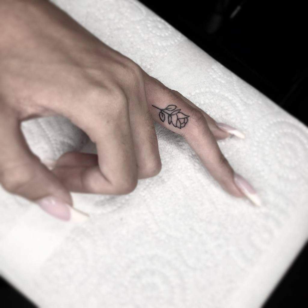Minimalist black rose tattoo on the side of the finger, featuring fine-line details