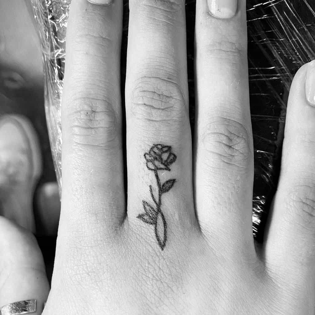 A delicate rose tattoo on the middle finger
