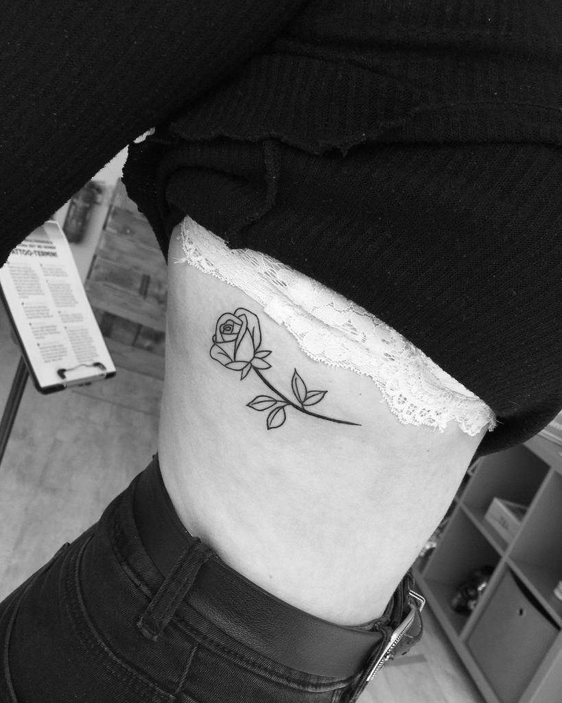 Black and white image of a simple rose tattoo on a woman's ribcage