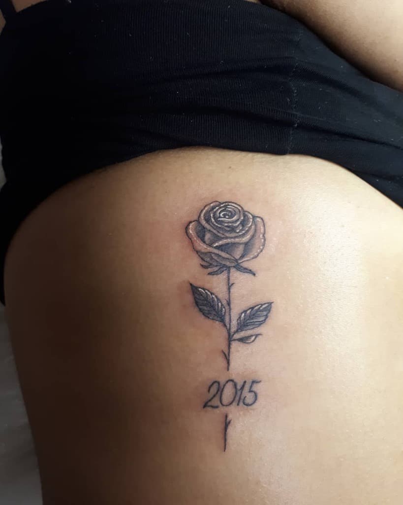 Tattoo of a rose with two leaves and the year "2015" on a person's skin