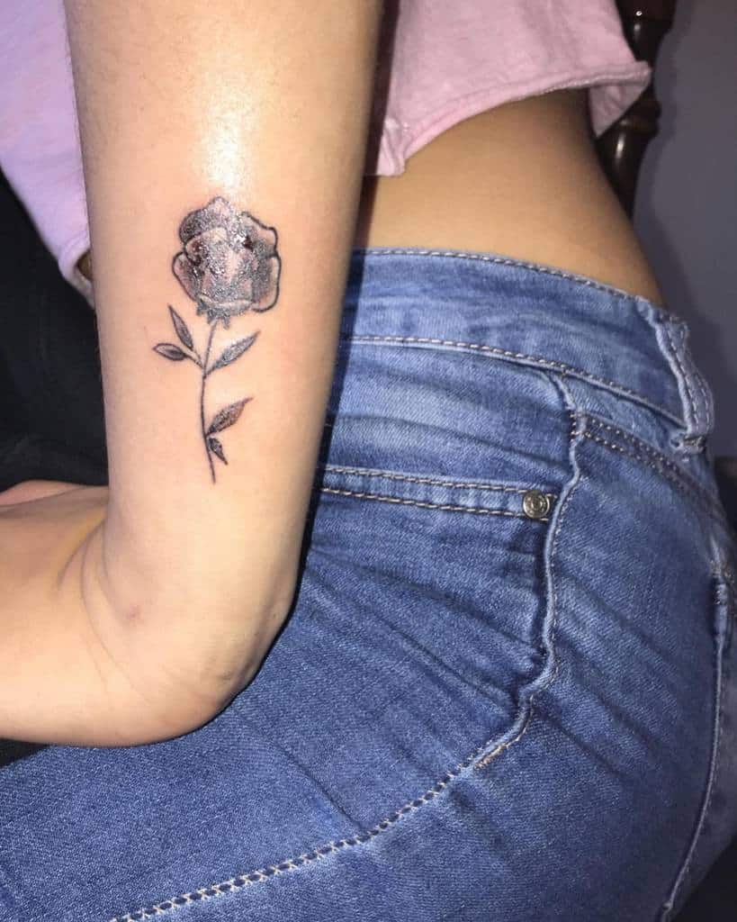 Black and grey rose tattoo on the forearm, featuring delicate shading and fine-line details