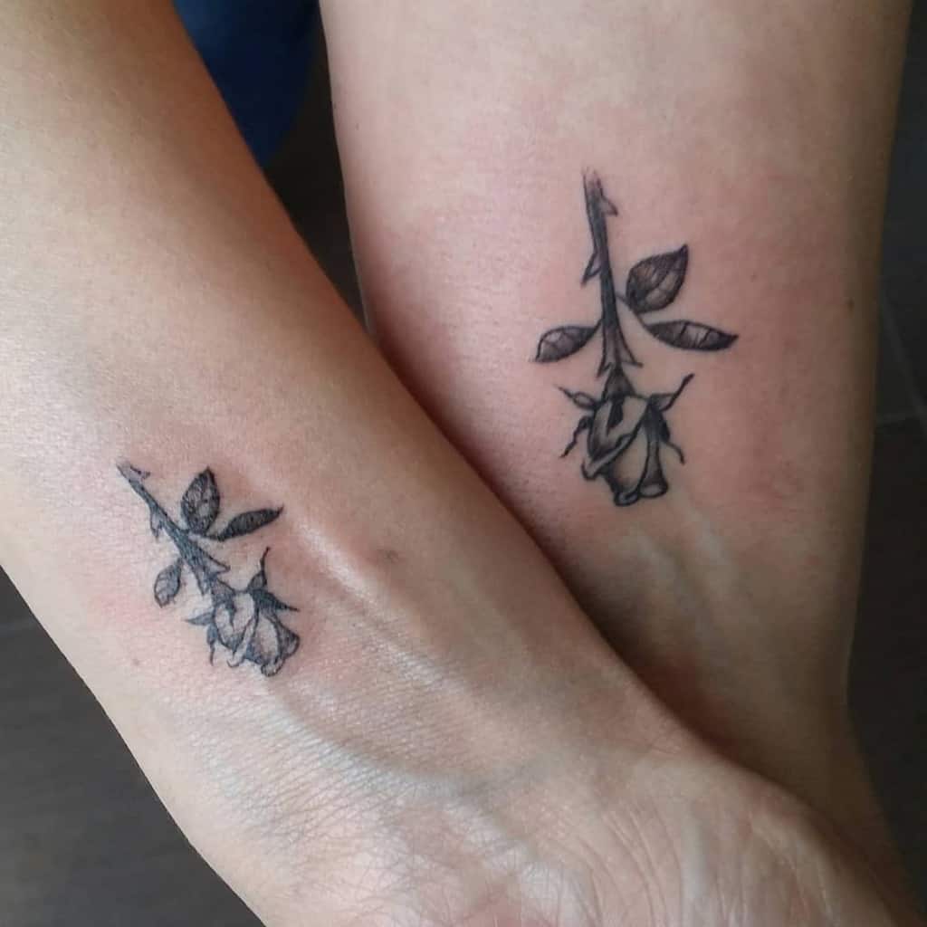 Two wrists with matching black ink tattoos of a rose with leaves