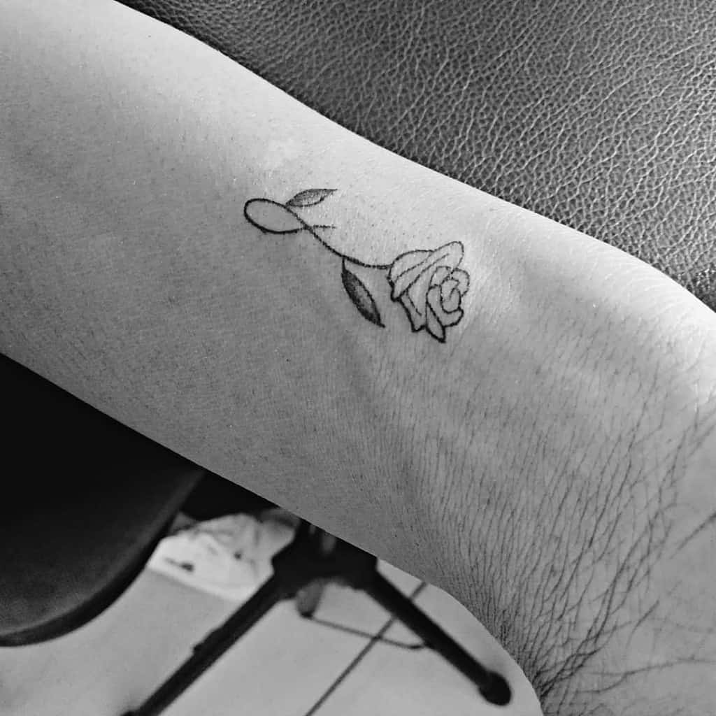 A small rose tattoo on a wrist, in black ink, with a minimalist design