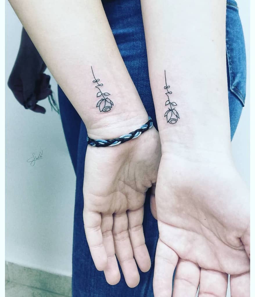Two arms with matching minimalist rose tattoos on the inner wrists