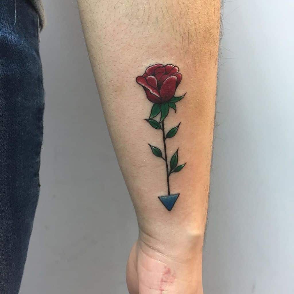 A tattoo of a red rose with green leaves and a blue downward arrow on a forearm