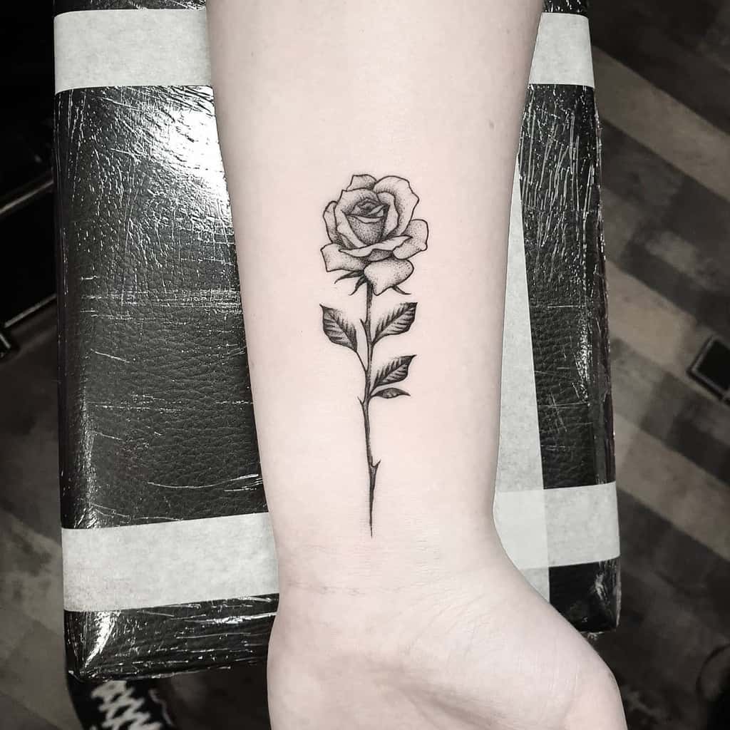Tattoo of a detailed rose with a long stem on a wrist