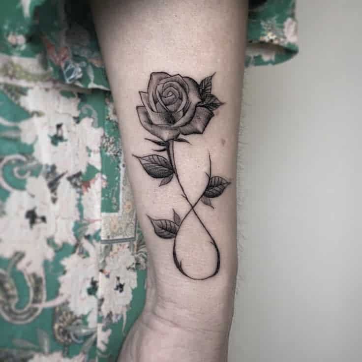 Black and gray tattoo of a rose with leaves, forming an infinity symbol on an arm