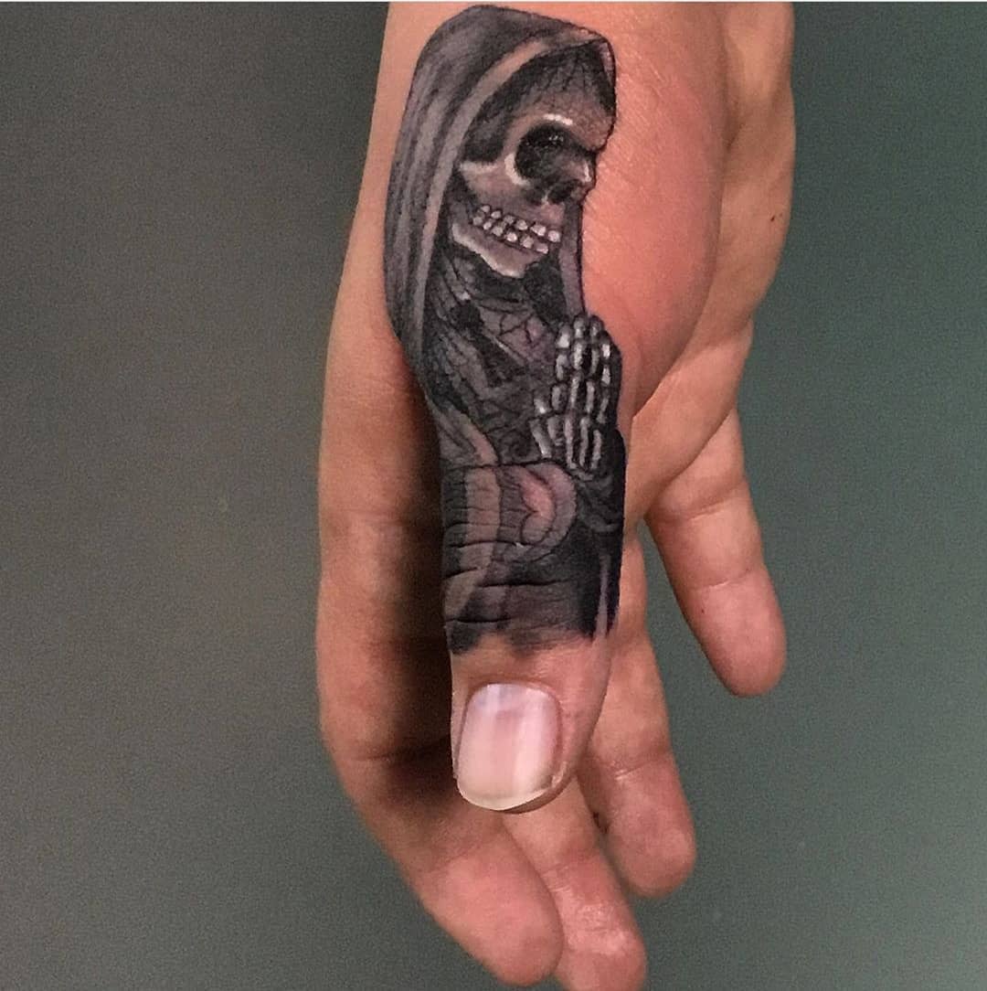 Small Santa Muerte tattoo depicted on the side of a finger, showcasing a detailed skeleton figure in prayer