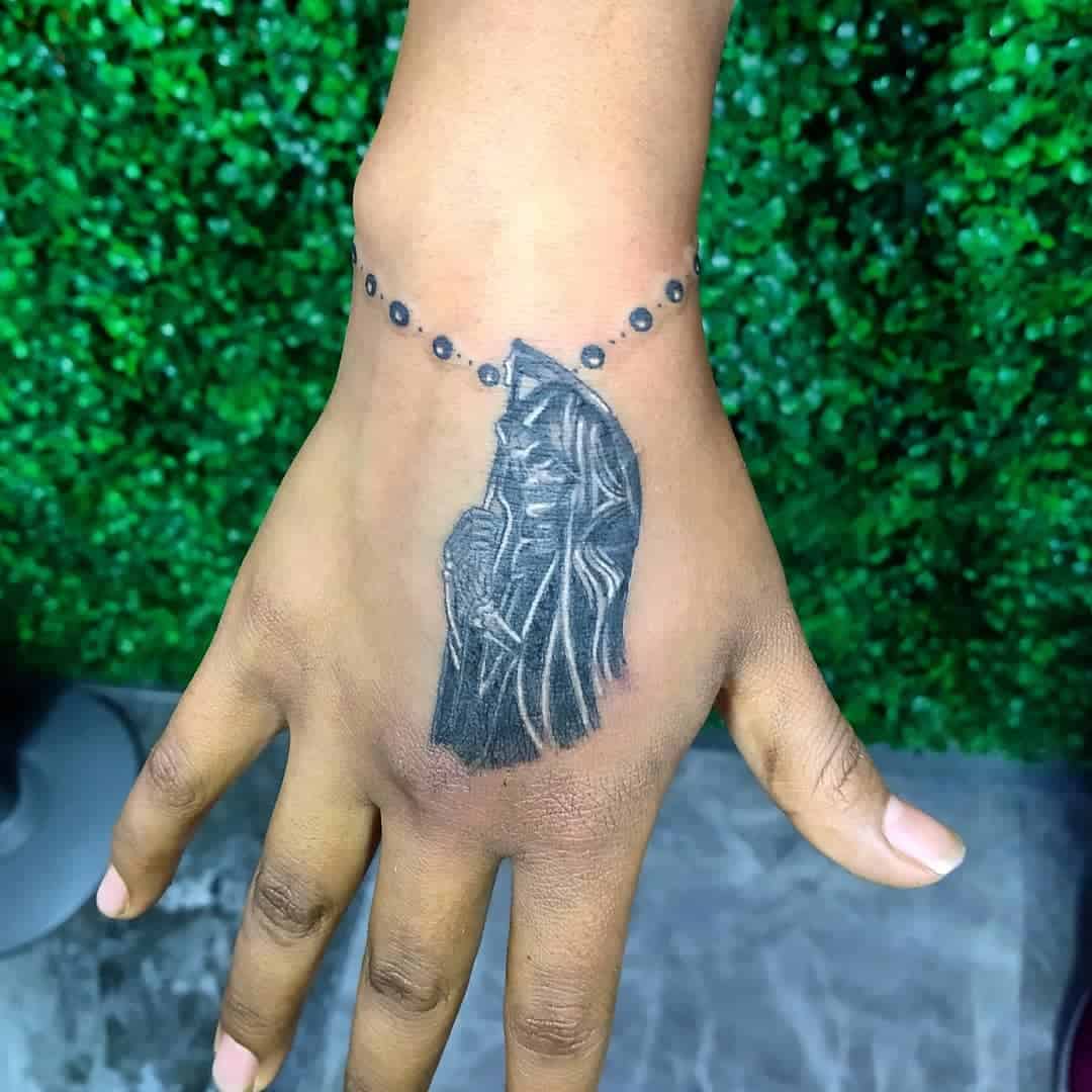 Small Santa Muerte hand tattoo with rosary bracelet, featuring subtle shading and intricate details