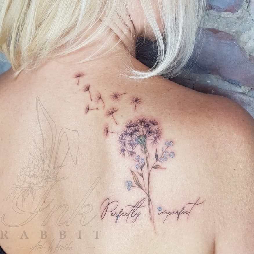 Woman's back tattoo with dandelion flowers and seeds; text reads "Perfectly imperfect" in cursive