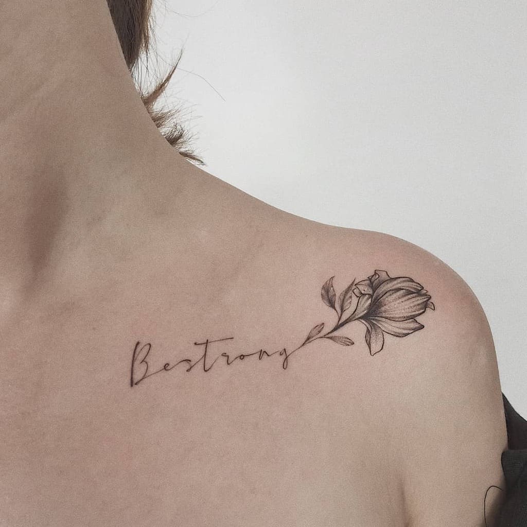 Tattoo of a flower and the word "Be strong" on a woman's shoulder