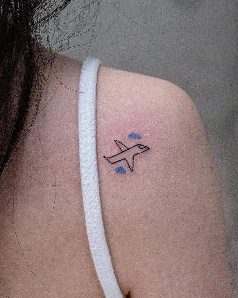 Small tattoo of an airplane with two blue clouds on a woman's shoulder