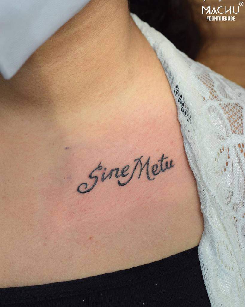 Tattoo on chest reads "Sine Metu" in cursive under a lace neckline
