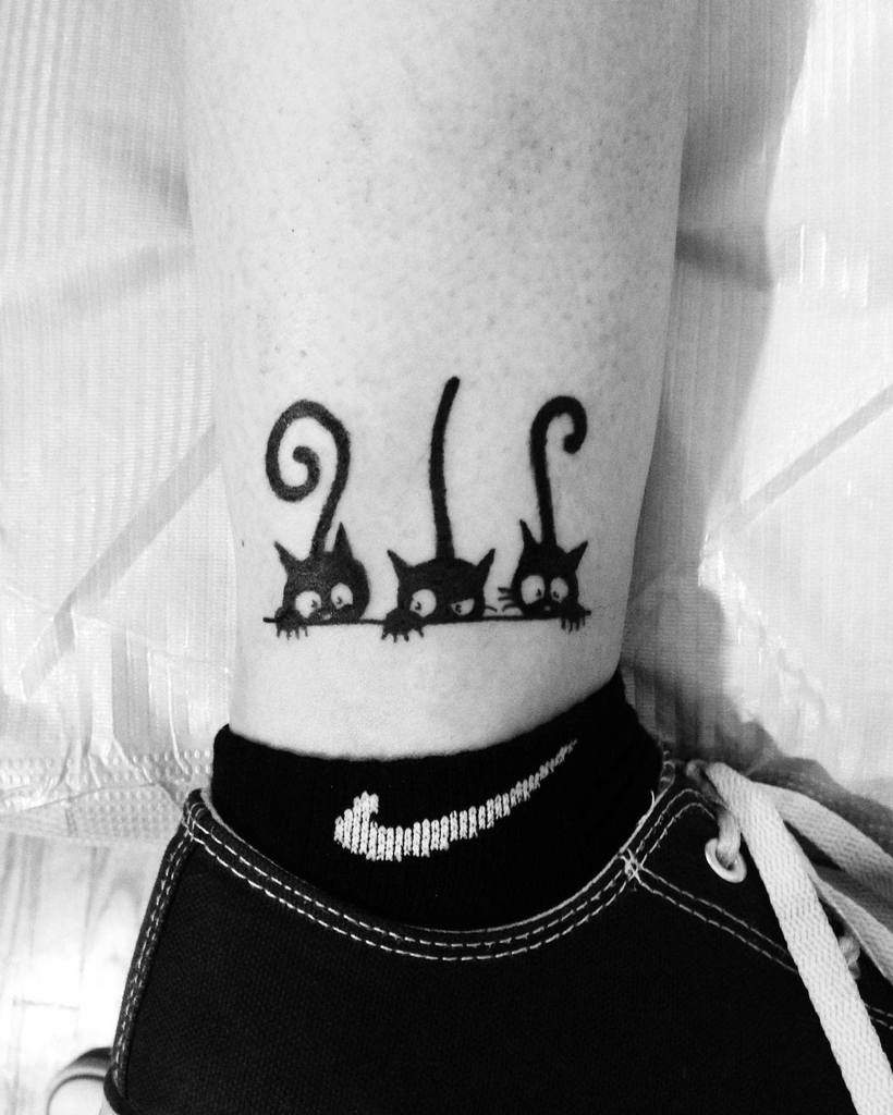 Tattoo of three black cats with curled tails on an ankle