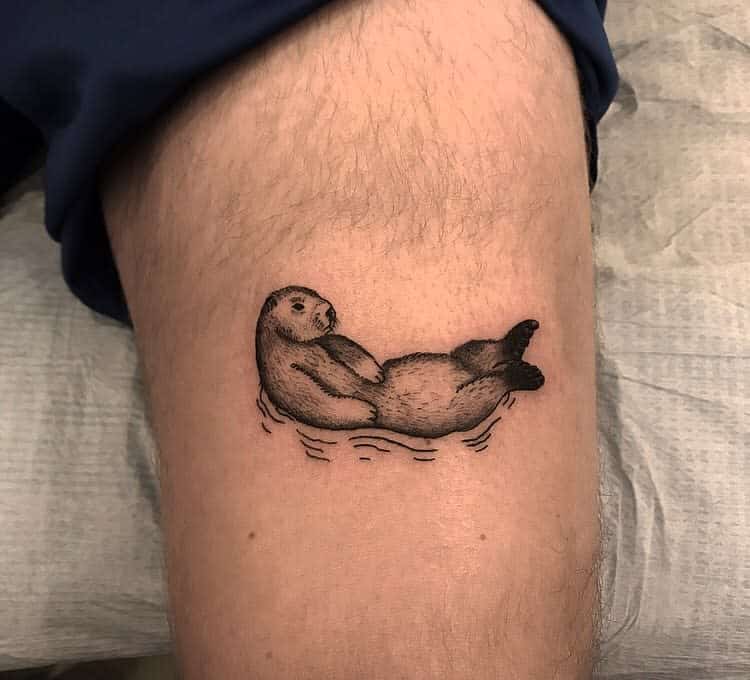 A detailed otter tattoo graces a person's leg, with the otter serenely floating on its back