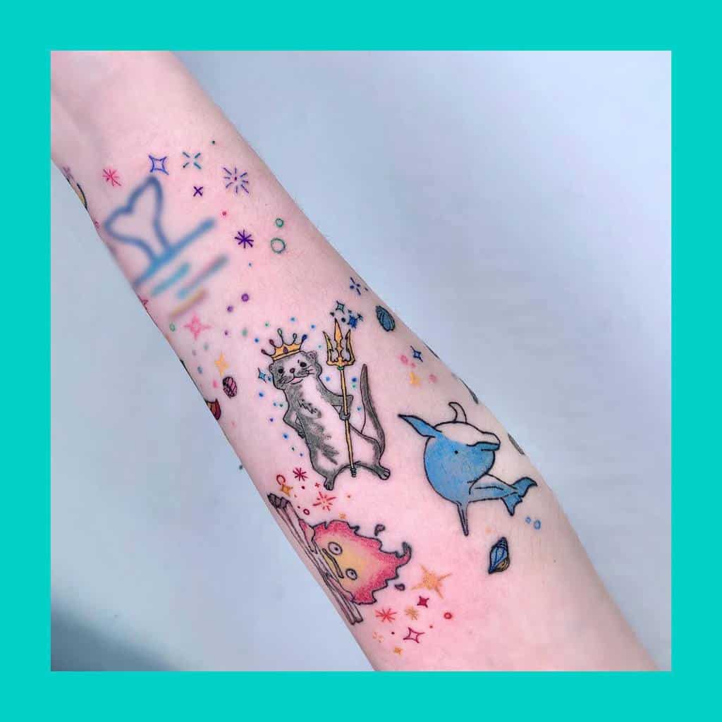 Colorful whimsical tattoos on an arm, featuring an otter with a cat wielding a trident, a narwhal, and various stars and shapes