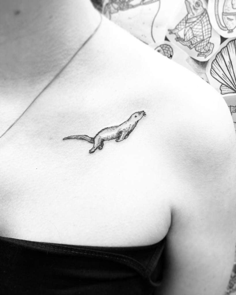 Black and white photo of a minimalist otter tattoo adorning a person's upper chest near the collarbone