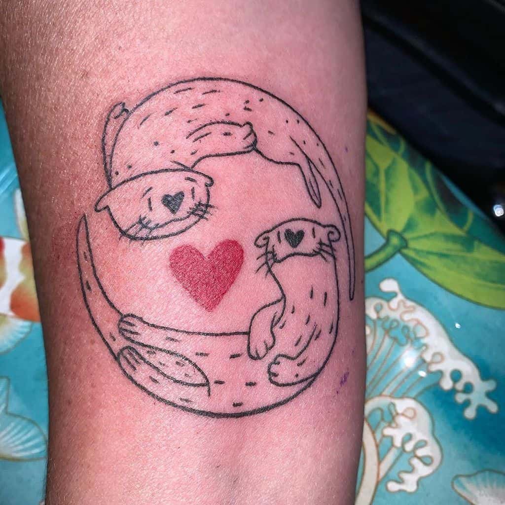 Two otters circle tattooed on skin, each with a heart on its head, enclosing a larger red heart in the center