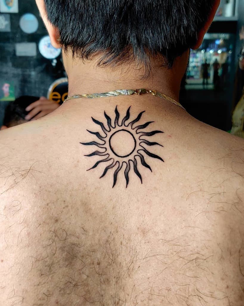 A black sun tattoo with wavy rays on the upper back
