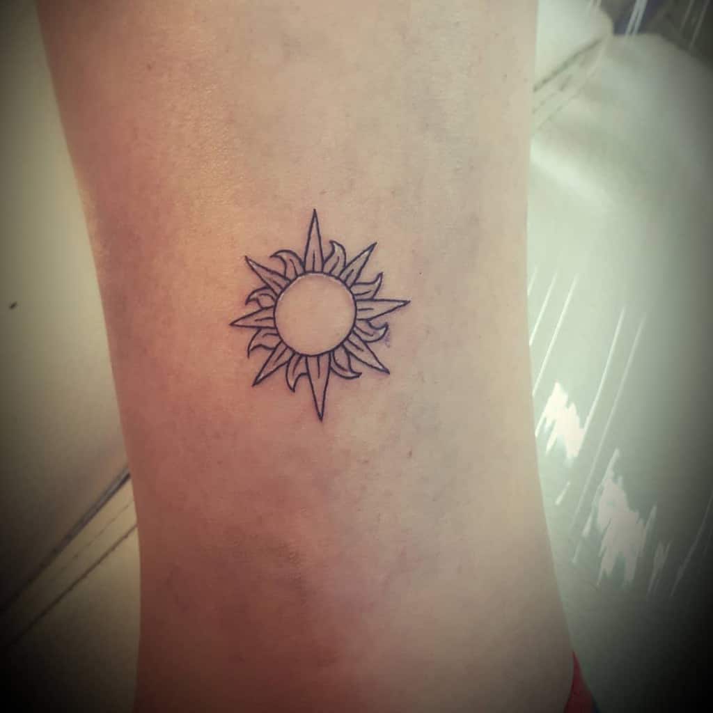 Small, simple sun tattoo with clean lines and pointed rays, placed on the ankle for a subtle yet classic design