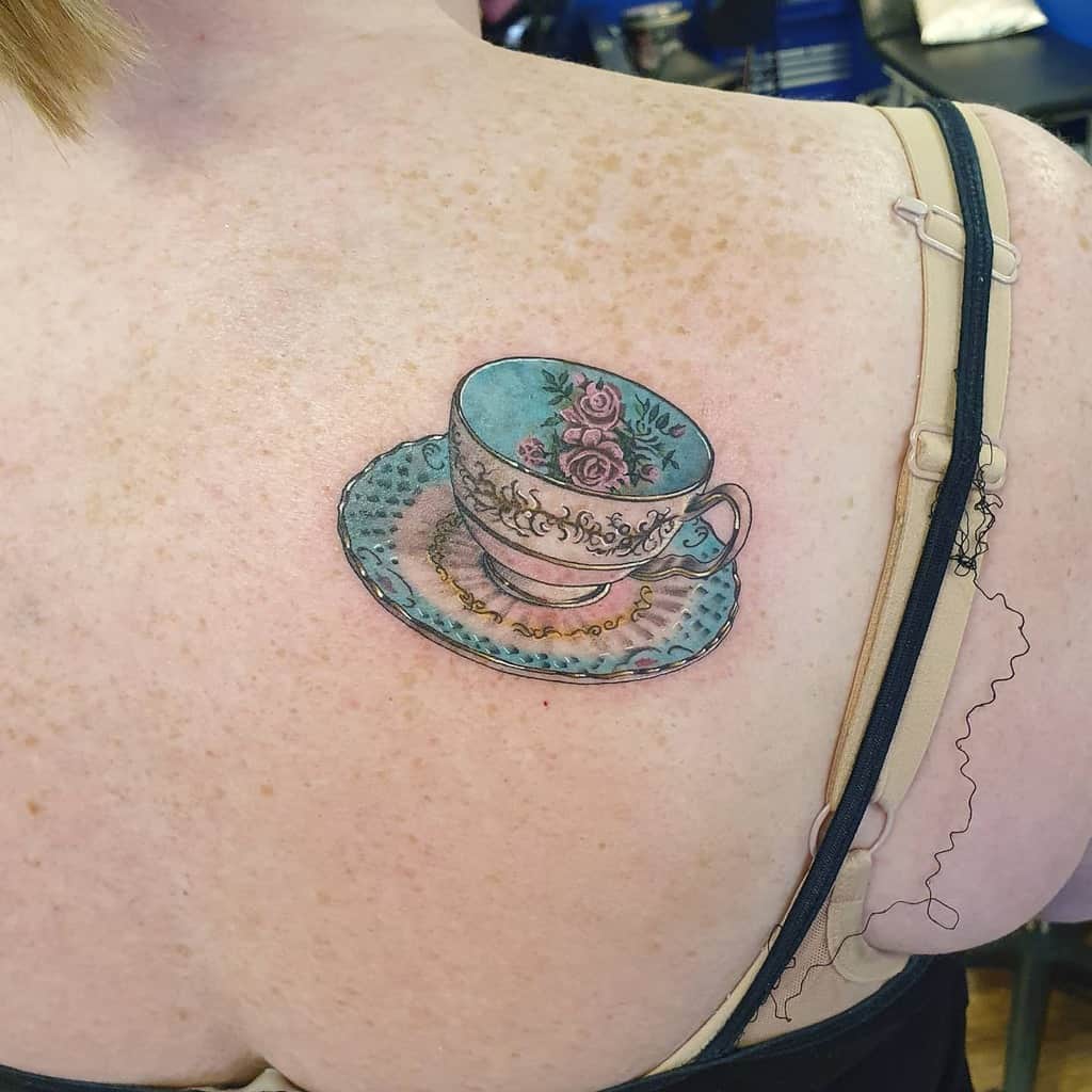Colorful tattoo of a vintage teacup with blue floral patterns and gold detailing, resting on a matching saucer