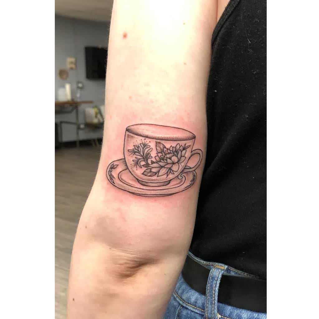 Fine-line black and grey tattoo of a vintage teacup on a saucer, featuring intricate floral designs for an elegant and delicate look