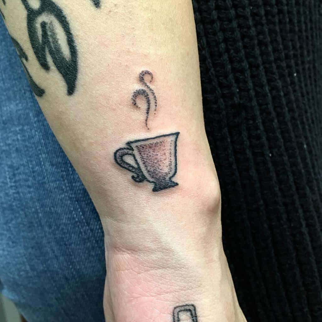 Minimalist black and grey tattoo of a small steaming teacup, featuring subtle shading and a delicate design