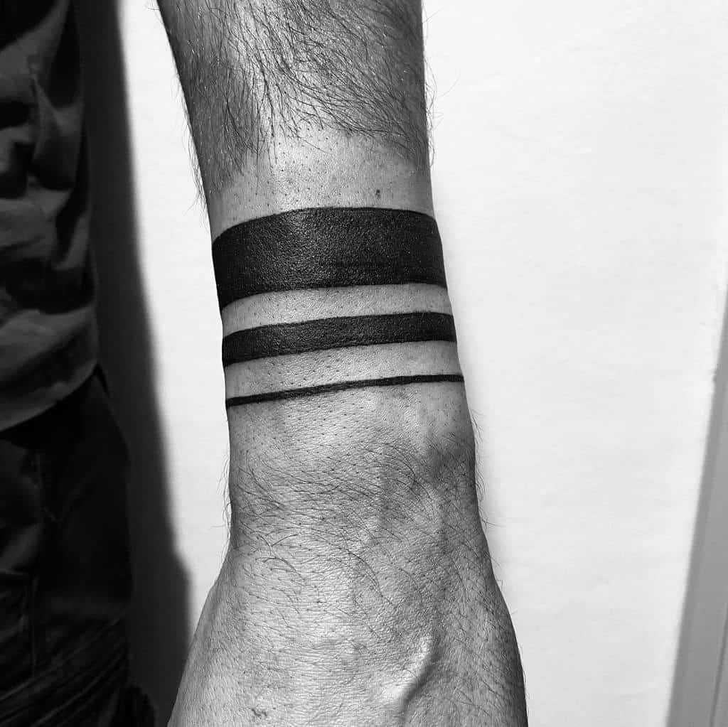 The tattoo features three bold horizontal black stripes around the forearm, creating a minimalist and striking design with clean lines and a solid finish