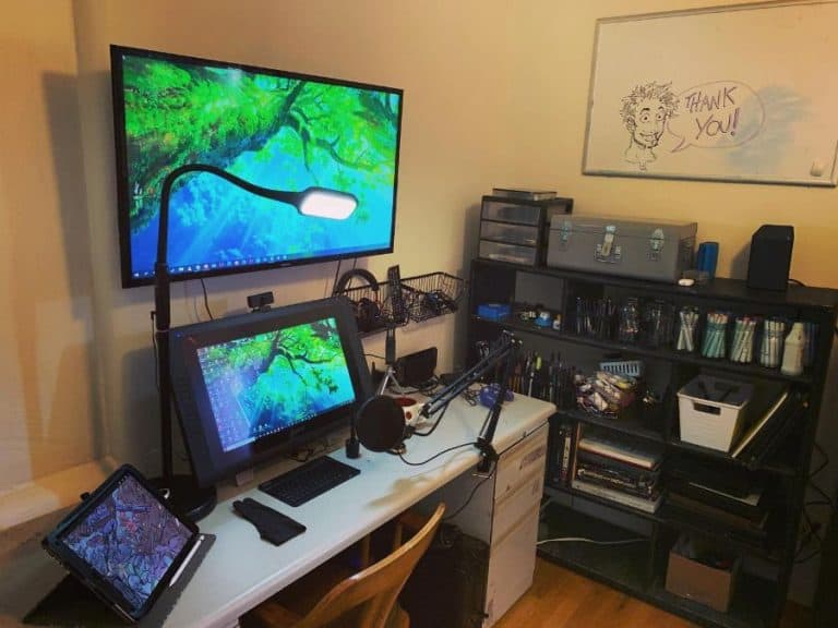 A home office setup with multiple screens, a microphone, tablet, and organized shelves. A whiteboard says "Thank you!