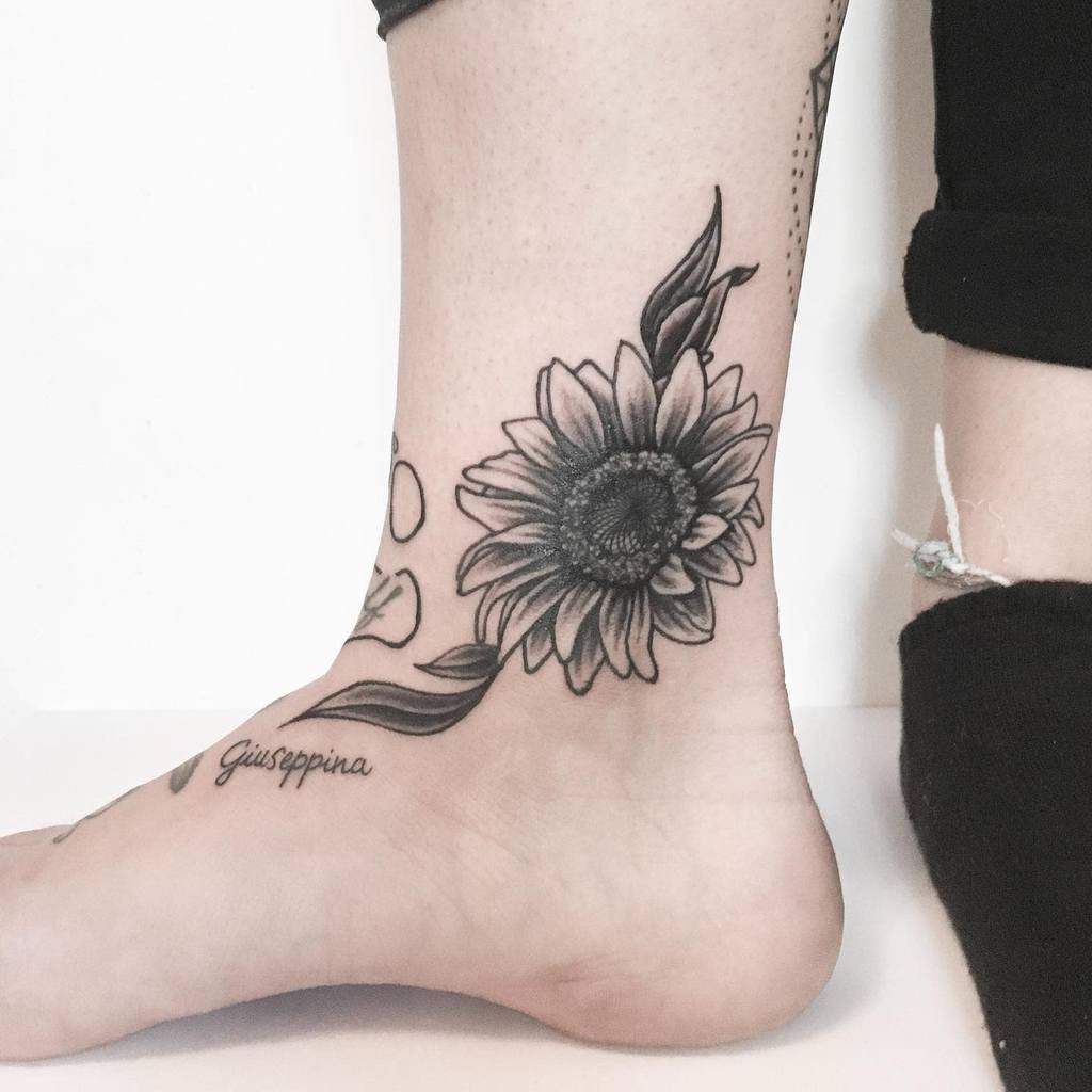Tattoo of a sunflower and script on an ankle and foot