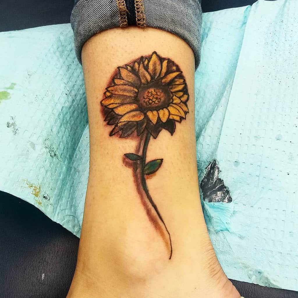 Sunflower tattoo on a person's ankle with a vibrant yellow and green color palette