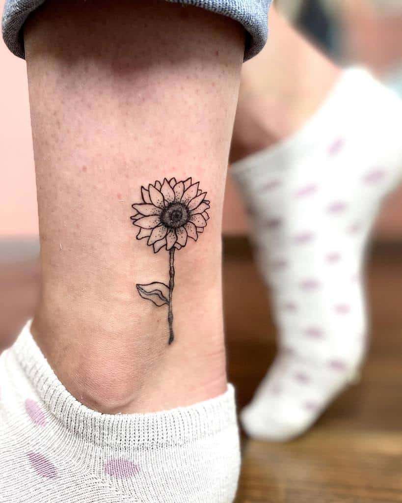 Small black line sunflower tattoo on an ankle
