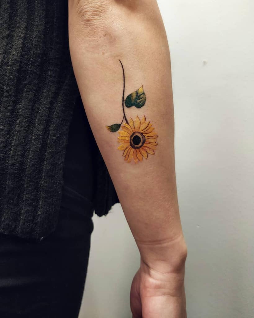 A sunflower tattoo with green leaves on a forearm