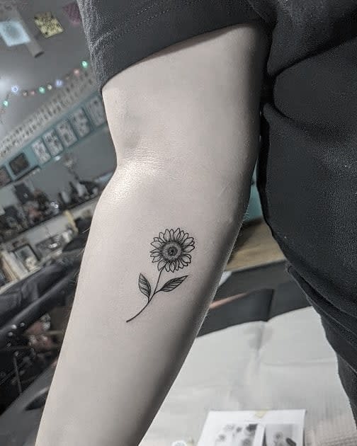 Small black and white tattoo of a sunflower on an arm