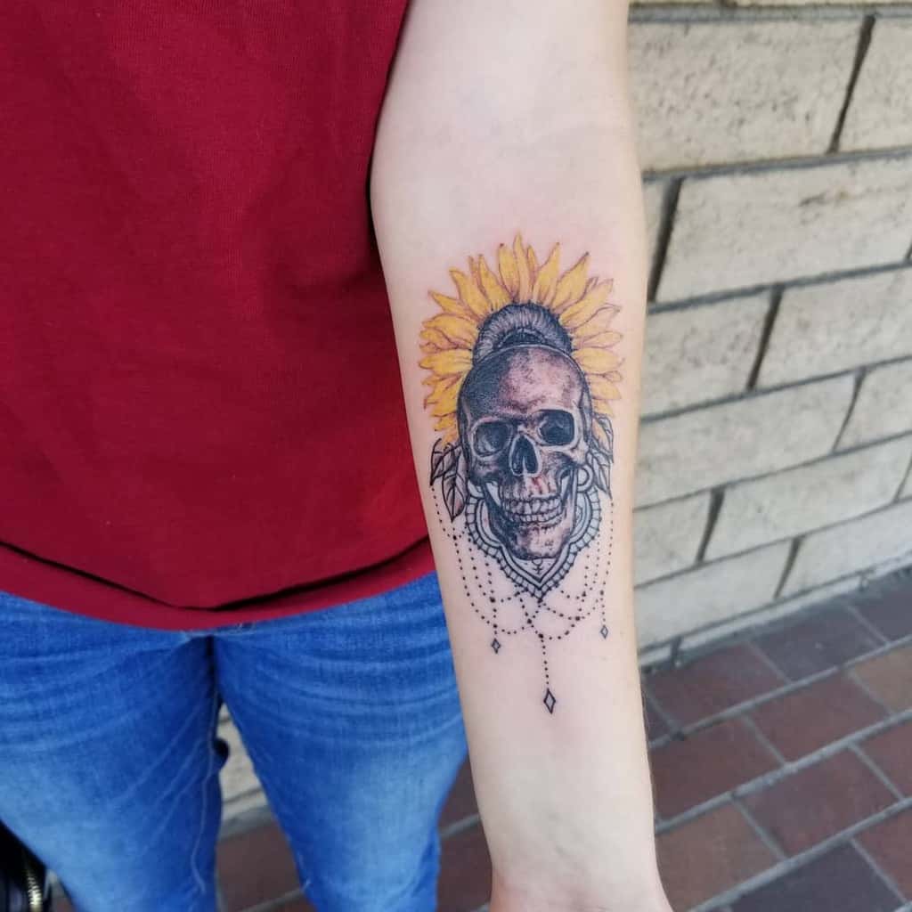 Forearm tattoo of a skull with a yellow sunflower and decorative elements around it