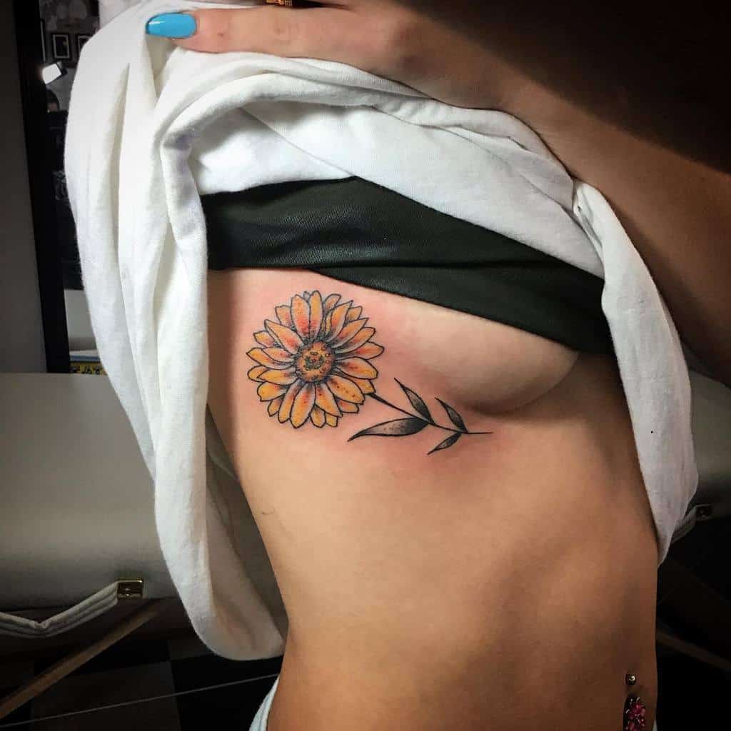 A yellow flower tattoo with leaves on a person's ribcage