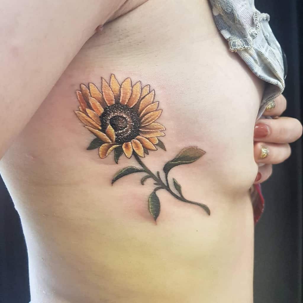Sunflower tattoo on a person's side, with detailed petals and leaves