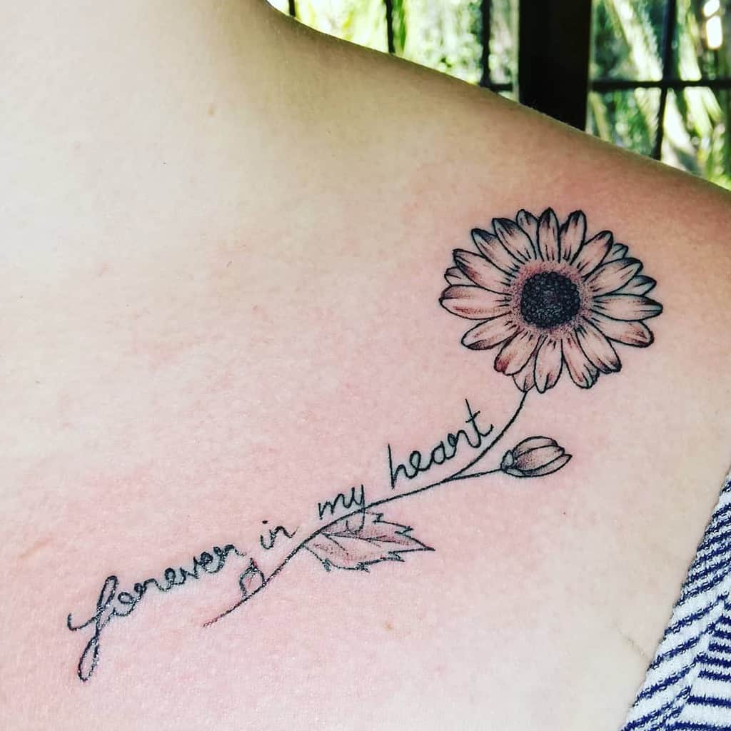 Tattoo of a sunflower and script reading "Forever in my heart" on a shoulder