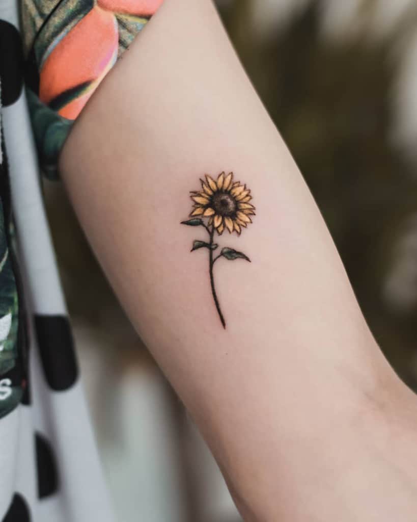 Small sunflower tattoo on a forearm with yellow petals and green leaves
