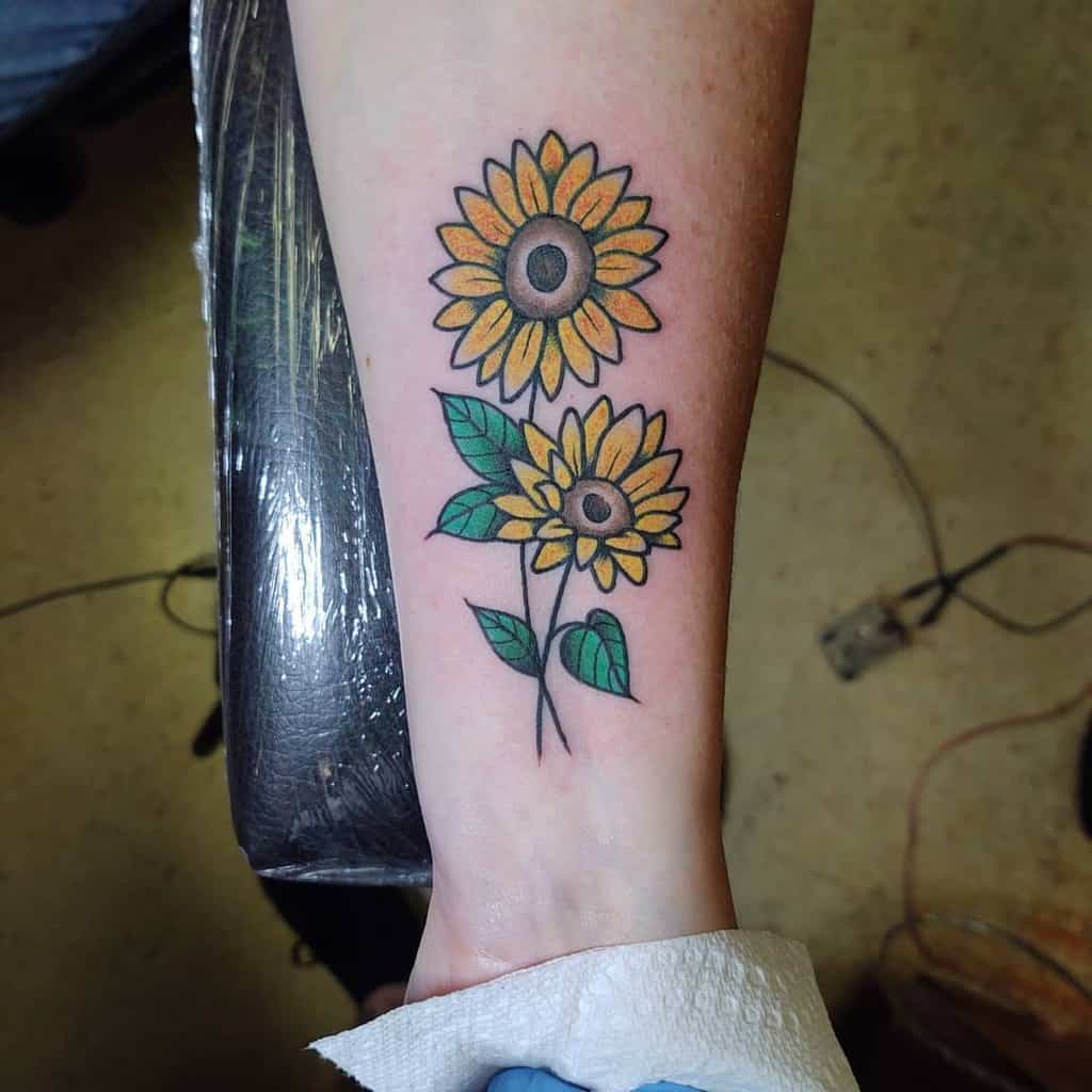 A forearm tattoo of two sunflowers with green leaves