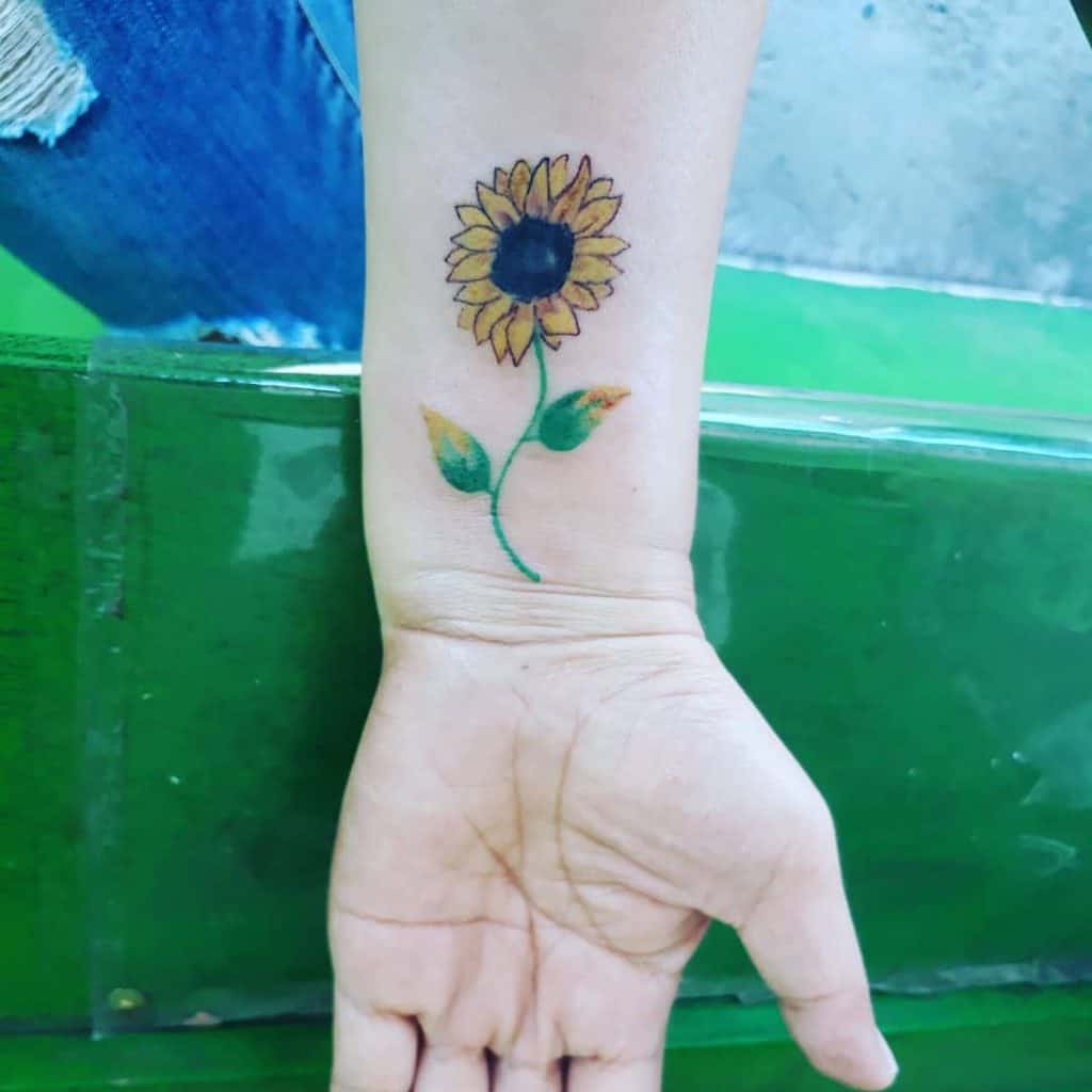 Wrist with a colorful sunflower tattoo, showing detailed petals and leaves