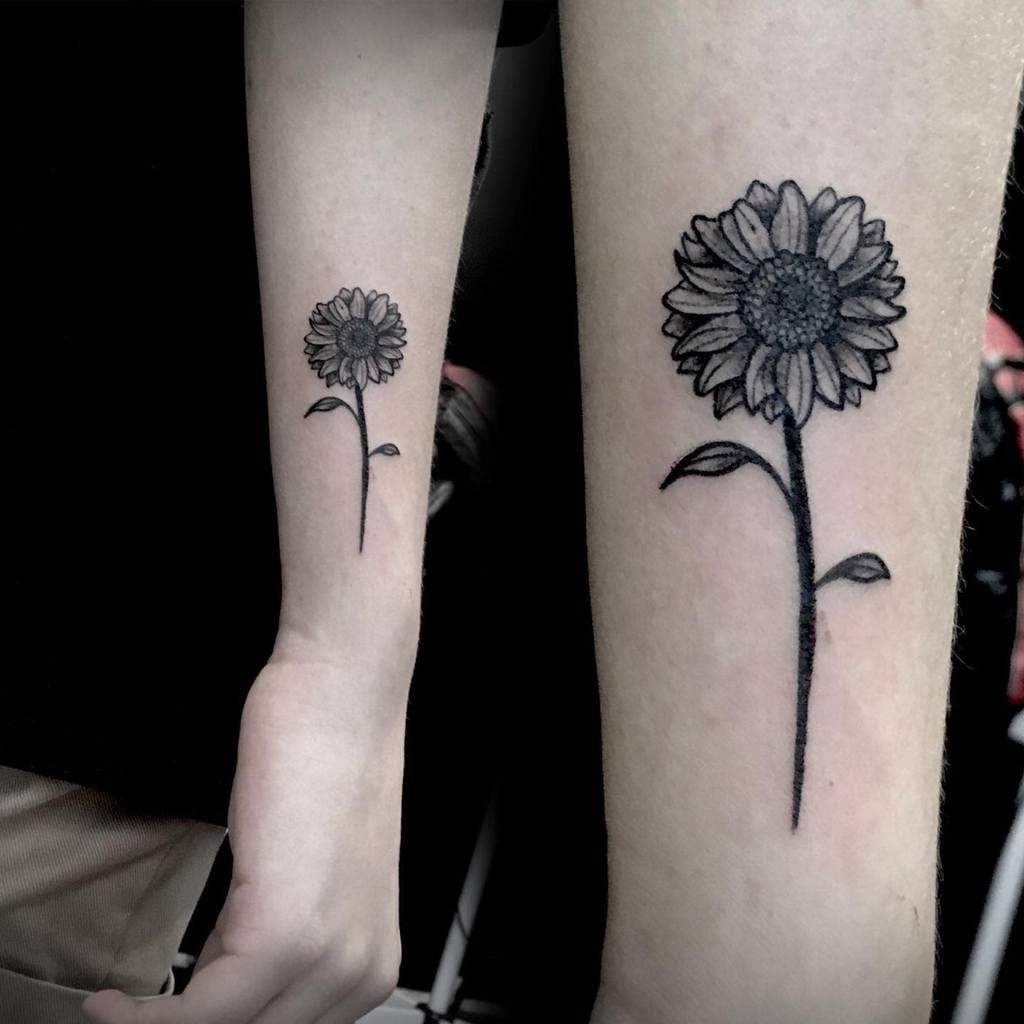 Two forearms displaying matching sunflower tattoos with detailed petals and leaves
