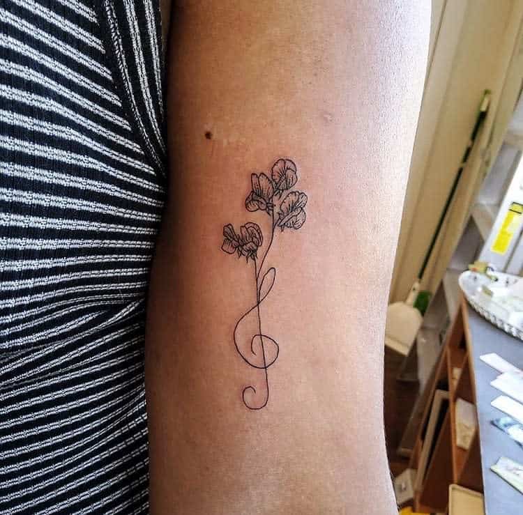 A sweet pea flower tattoo with a treble clef stem, blending music and nature in a unique design