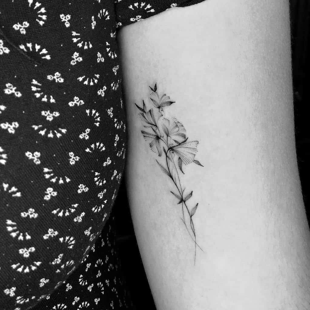 A beautifully shaded sweet pea tattoo on the upper arm, creating a soft and elegant floral design