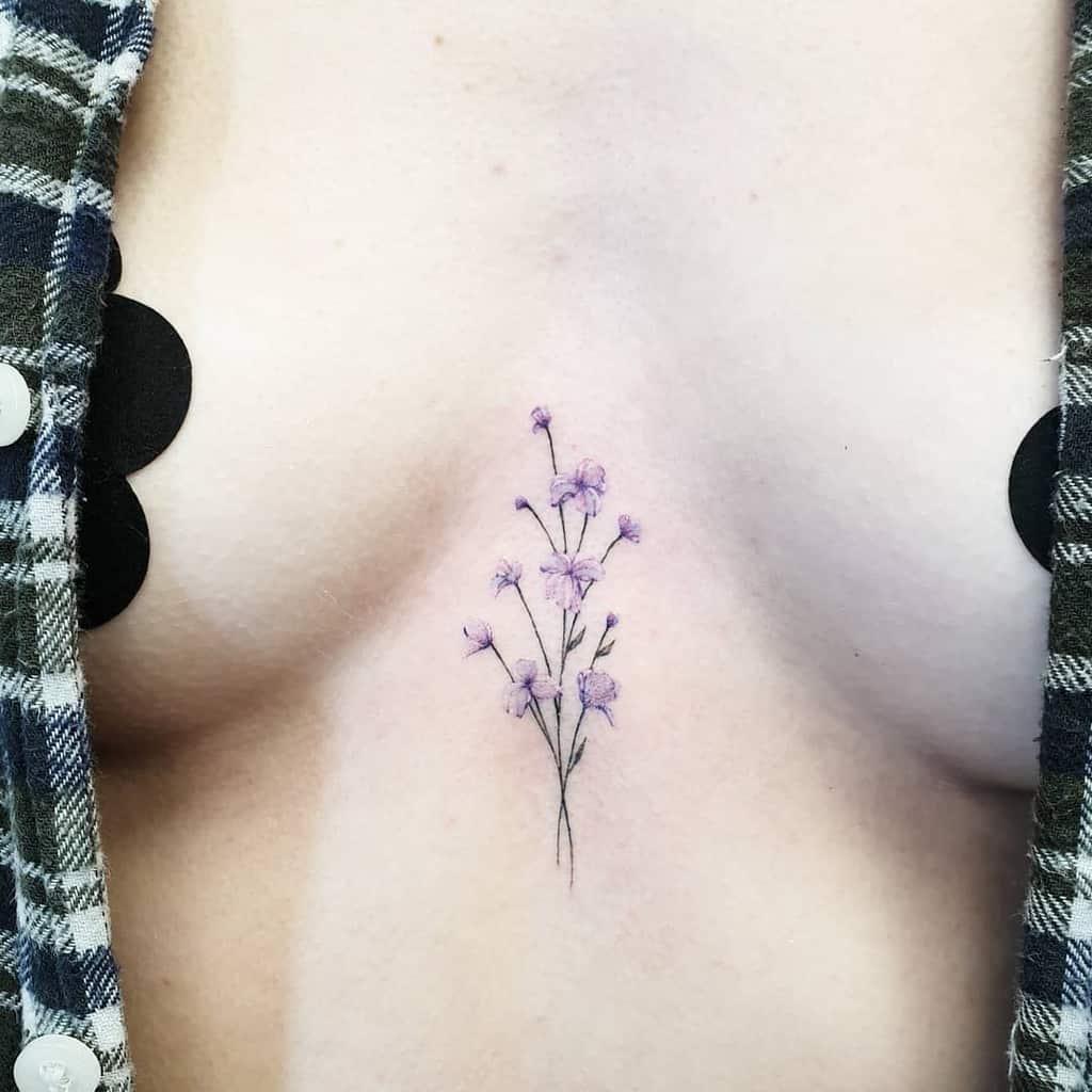 A minimalistic sweet pea tattoo with delicate purple flowers, positioned in the center of the chest