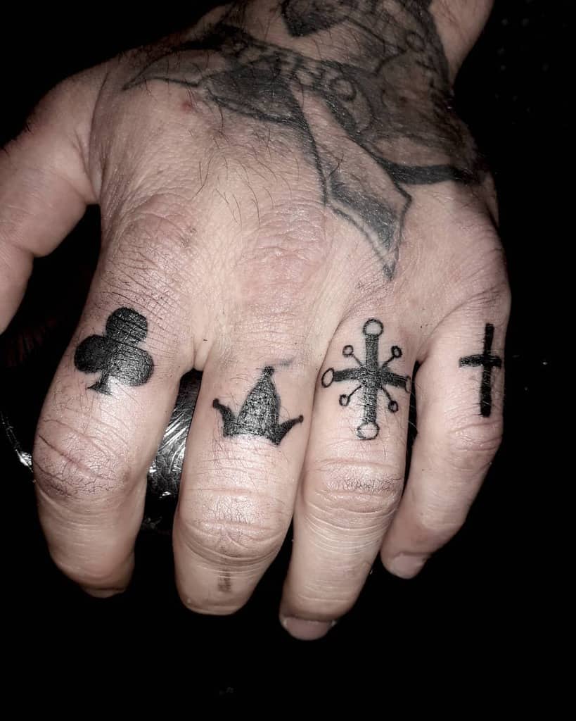 Hand with tattoos of club, crown, six-pointed symbol, and cross on fingers