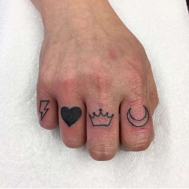 Fingers with tattoos: lightning bolt, heart, crown, and crescent moon