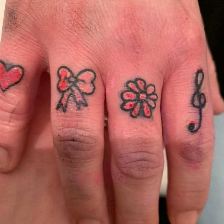 Fingers with tattoos: heart, bow, flower, and musical note