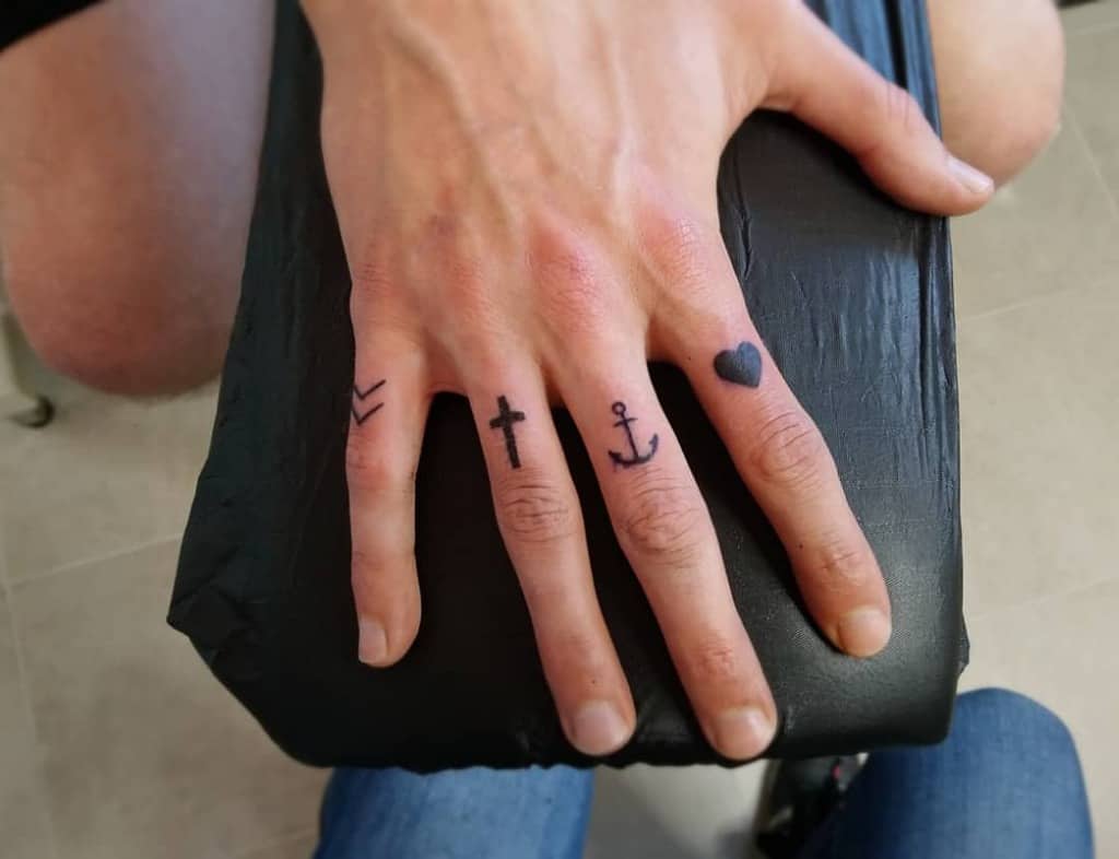 Minimalist finger tattoos featuring a chevron, cross, anchor, and heart, symbolizing direction, faith, stability, and love