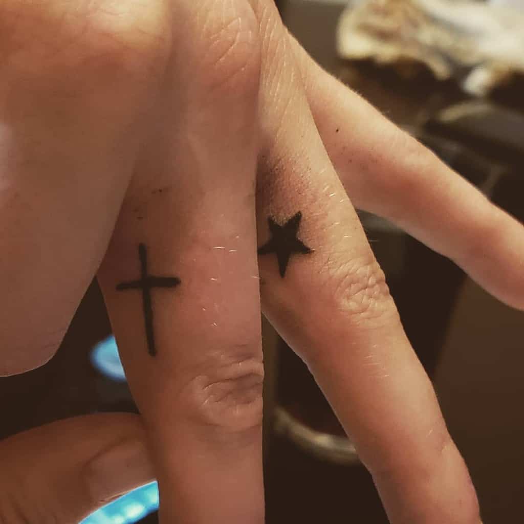 Fingers with a cross tattoo on one and a star tattoo on the other